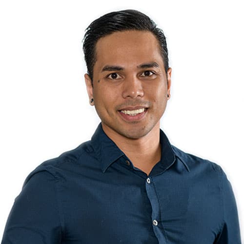 A man with short dark hair, wearing a dark blue button-up shirt, smiles at the camera against a plain white background.